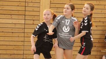 Drei Kinder im Jugendhandball im Zweikampf während eines Spiels in der Sporthalle, körperbetonte Spielsituation im Nachwuchs-Handballverein