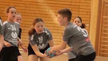 Zwei Kinder im Jugendhandball beim Zusammenspiel mit Ball in der Sporthalle, Teamaktion im Nachwuchs-Handballverein