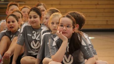 Junge Spielerinnen sitzen hintereinander auf dem Hallenboden