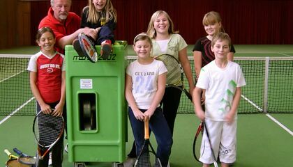 Tennismannschaft Kinder lachen in Kamera neben Ballwurfmaschine
