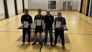 Vier Tischtennisspieler stehen mit Urkunden vor einer Tischtennisplatte in der Sporthalle, Auszeichnung bei einem Vereinswettkampf